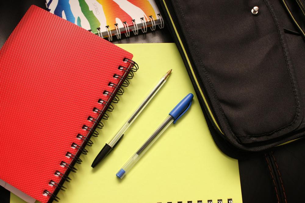 red and yellow notebooks and black and blue pens and other school supplies